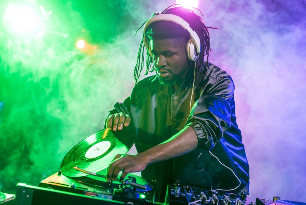 professional african american DJ in headphones with sound mixer in nightclub